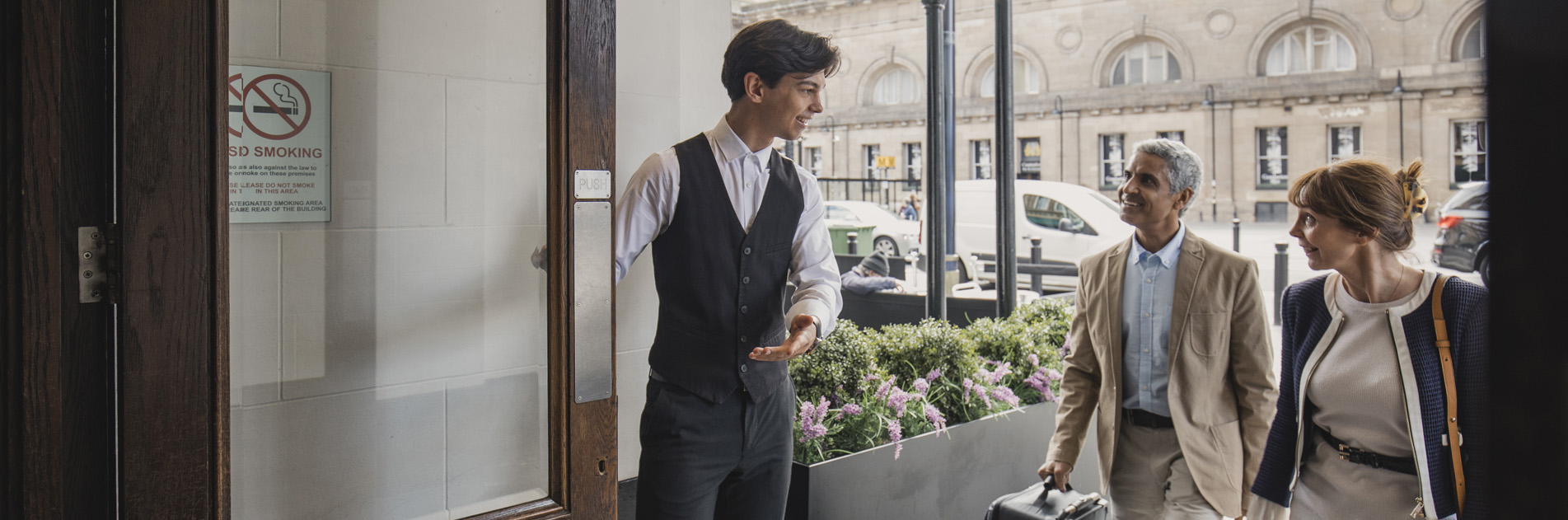 Staff opening hotel lobby door for guests